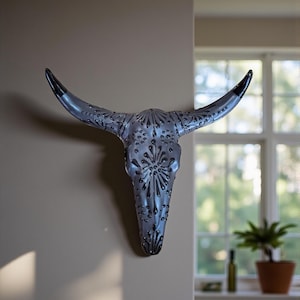 A decorative black Talavera  longhorn skull wall hanging. The skull features intricate embossed detailing and black-tipped horns. The wall art is mounted on a neutral-colored wall, adding a rustic touch to the decoration