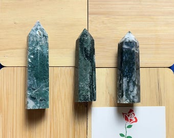 May include: Three green and white agate crystal points on a wooden surface. The points are all different sizes and shapes.