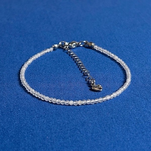 May include: A delicate white beaded bracelet with a silver heart charm and a silver clasp.