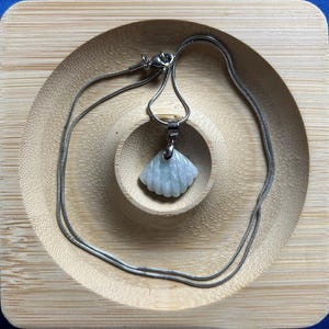 Pode incluir: Um colar de corrente de prata com um pingente de concha de jade branco. O pingente é esculpido em forma de leque.