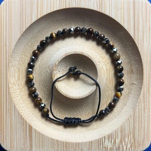 May include: A brown and black beaded bracelet with a black cord closure. The beads are made of tiger's eye and hematite.