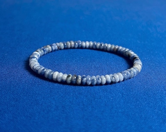May include: A blue gemstone bracelet made of small, round beads. The bracelet is on a blue background.