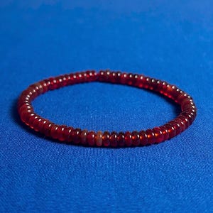May include: A red beaded bracelet on a blue background.