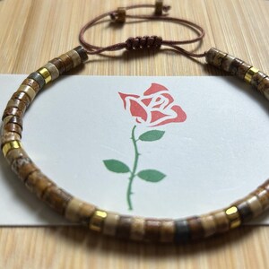 May include: A brown and gold beaded bracelet with a brown leather cord and a sliding knot closure.