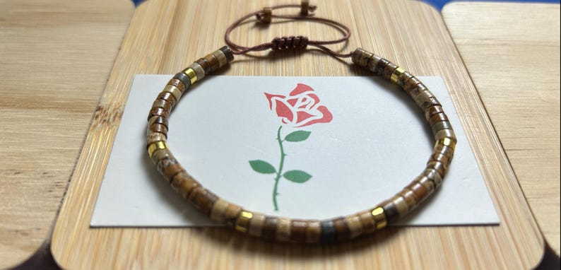 May include: A brown and gold beaded bracelet with a brown leather cord and a sliding knot closure.