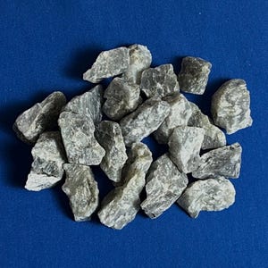 Puede incluir: Una colección de piedras pulidas grises y blancas. Las piedras son lisas y tienen una textura natural y rugosa.