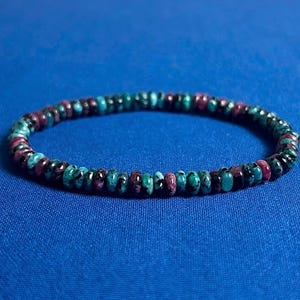 May include: A bracelet made of small, round beads in shades of turquoise, black, and pink.
