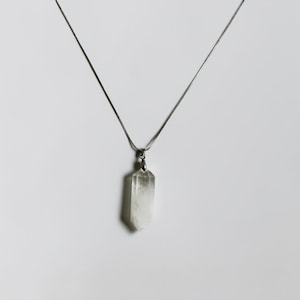 May include: A clear, hexagonal, double-terminated quartz crystal pendant suspended from a thin, silver-toned metal chain. The crystal is translucent with natural internal inclusions and is secured by a small, polished silver-toned metal bail.