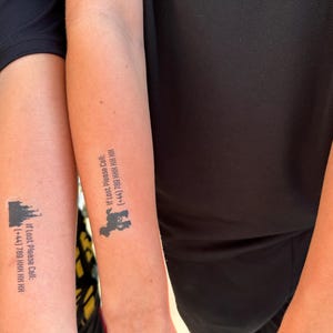 May include: Three forearms each featuring a black temporary tattoo. Each tattoo displays a small black silhouette of a castle or animal above the text: If Lost Please Call: (+44) 789 HHH HH HH. The tattoos are applied to the skin of three individuals.