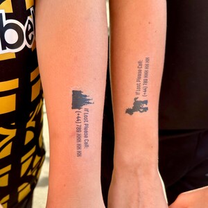 May include: Two temporary tattoos on skin. The left tattoo features a black castle silhouette with the text: If Lost Please Call: (+44) 789 HHH HH HH. The right tattoo shows a black cartoon character silhouette with the text: If Lost Please Call: (+44) 789 HHH HH HH.