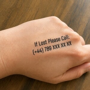May include: A temporary tattoo applied to the skin featuring black text that reads: If Lost Please Call: (+44) 789 XXX XX XX. The lettering is printed in a clean, sans-serif font, providing a clear and legible message for identification purposes.