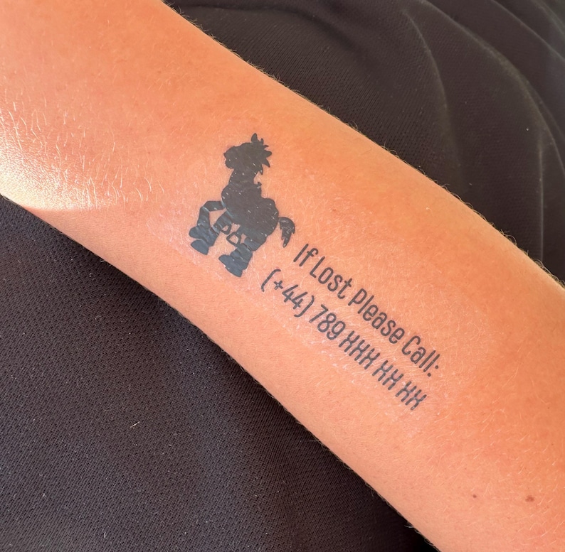 May include: A black temporary tattoo featuring a stylized horse icon positioned above the text "If Lost Please Call: (+44) 789 XXX XX XX". The design is applied to skin, displaying a clear, dark ink graphic with a bold, sans-serif typeface.