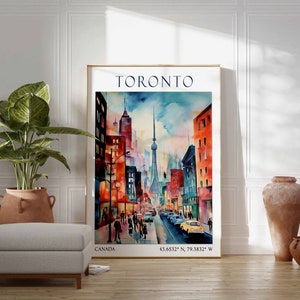Op de afbeelding: Een aquarel van de skyline van Toronto, met de CN Tower en andere gebouwen in een levendig palet van rood, oranje, geel, blauw en groen. Het schilderij is ingelijst en heeft de tekst "TORONTO" en "CANADA" boven en onder, respectievelijk. De co&ouml;rdinaten "43.6532&deg; N, 79.3832&deg; W" zijn ook opgenomen.