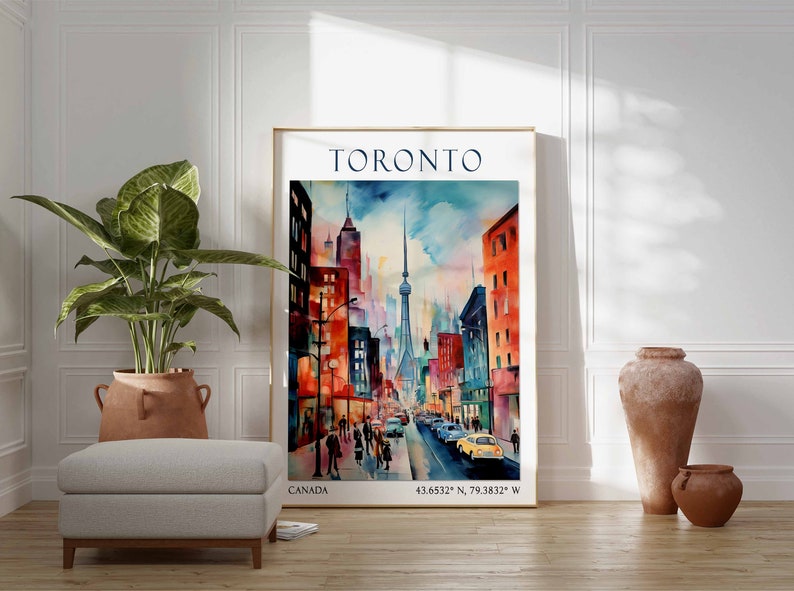 Op de afbeelding: Een aquarel van de skyline van Toronto, met de CN Tower en andere gebouwen in een levendig palet van rood, oranje, geel, blauw en groen. Het schilderij is ingelijst en heeft de tekst "TORONTO" en "CANADA" boven en onder, respectievelijk. De co&ouml;rdinaten "43.6532&deg; N, 79.3832&deg; W" zijn ook opgenomen.