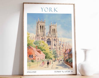 May include: A framed watercolor print of York Minster in England. The artwork features the cathedral with a blue sky, buildings, and a street scene. Text at the top reads "YORK" and at the bottom "ENGLAND" with coordinates.