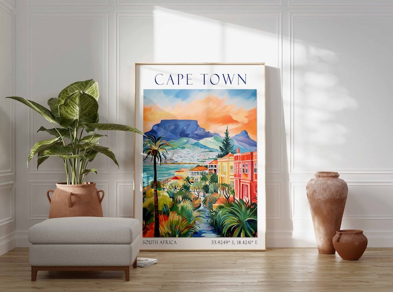 May include: A colorful vintage travel poster featuring a scenic view of Cape Town, South Africa. The poster depicts Table Mountain, palm trees, and colorful buildings. The text "CAPE TOWN" is displayed in a bold blue font at the top of the poster. The coordinates "33.9249&deg; S, 18.4241&deg; E" are displayed at the bottom of the poster.