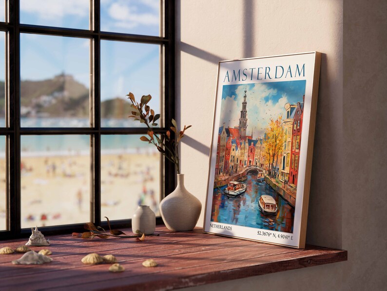 May include: A framed vintage travel poster with a colourful illustration of Amsterdam, Netherlands. The poster features a canal with boats, buildings, and a tall church steeple. The text on the poster reads "AMSTERDAM, NETHERLANDS, 52.3678&deg; N, 4.9041&deg; E".