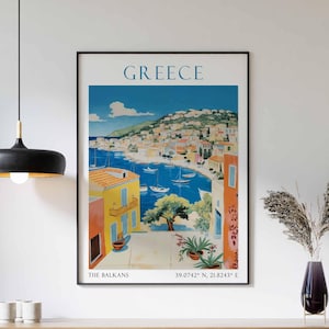 May include: A vintage travel poster for Greece featuring a colorful illustration of a seaside town with blue water, boats, and buildings. The poster includes the text "GREECE", "THE BALKANS", and "39.0742&deg; N, 21.8243&deg; E".