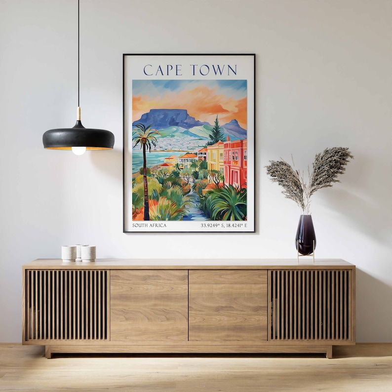 May include: A vintage travel poster featuring a colorful illustration of Cape Town, South Africa. The poster depicts a cityscape with Table Mountain in the background, palm trees, and colorful buildings. The text "CAPE TOWN" is displayed in a bold font at the top of the poster, with "SOUTH AFRICA" and coordinates below.