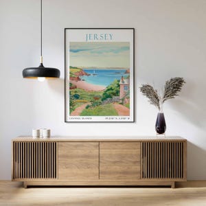 May include: A framed poster of Jersey, Channel Islands, showing a coastal scene with a sandy beach, turquoise sea, and a pink house. The poster has the word "JERSEY" at the top and coordinates at the bottom.