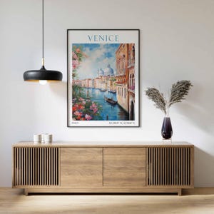 May include: A framed art print of Venice, Italy, featuring a canal scene with buildings, boats, and flowers. The word "VENICE" is at the top, with coordinates and "ITALY" at the bottom. The print is displayed above a wooden cabinet.