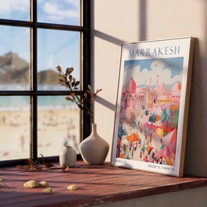 May include: A framed vintage travel poster with a colorful illustration of a city scene. The poster is titled "MARRAKESH" and includes the coordinates "31.6215&deg; N, 7.9984&deg; W".