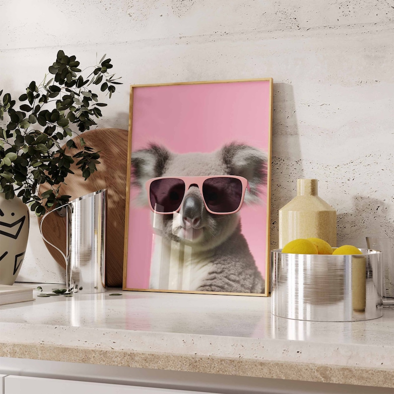May include: A framed print of a koala wearing pink sunglasses against a pink background. The koala is looking directly at the camera.