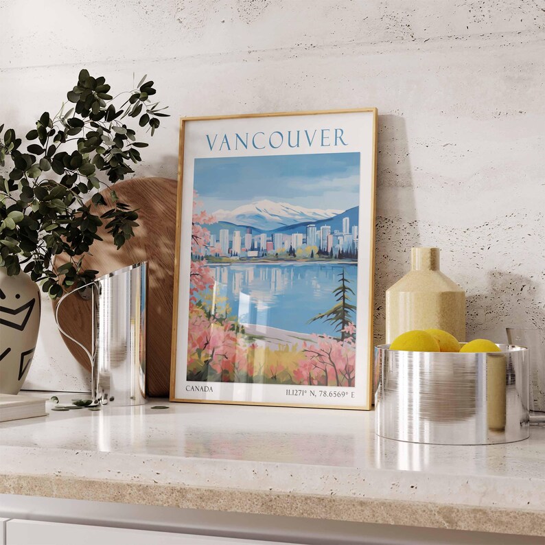 Puede incluir: Un p&oacute;ster vintage enmarcado con una ciudad y monta&ntilde;as en el fondo. El p&oacute;ster se titula "Vancouver" y tiene el texto "Canad&aacute;" y "49.27&deg; N, 78.6569&deg; E" en la parte inferior. El p&oacute;ster est&aacute; sobre una encimera con una jarra plateada, un jarr&oacute;n con limones amarillos y un taz&oacute;n plateado.