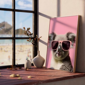 May include: A framed print of a koala wearing pink sunglasses against a pink background. The koala is looking directly at the camera with a relaxed expression.