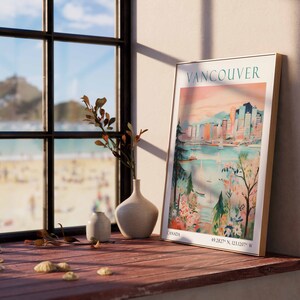 May include: A framed poster with a vintage travel illustration of Vancouver, Canada. The poster features a cityscape with buildings, a body of water, and boats. The poster is hanging on a wall next to a window with a view of a beach.