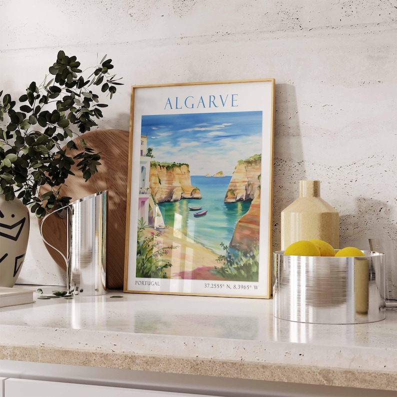 Pode incluir: Um poster emoldurado com uma pintura em aquarela de uma cena costeira no Algarve, Portugal. O poster tem o texto "ALGARVE" em uma moldura dourada. O poster est&aacute; em uma bancada branca com uma jarra de prata e uma tigela de prata com lim&otilde;es.