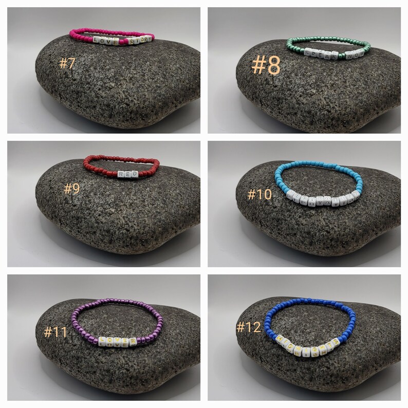 K&ouml;nnte beinhalten: Sechs bunte Perlenarmb&auml;nder mit wei&szlig;en Buchstabenperlen, die verschiedene W&ouml;rter buchstabieren. Die Armb&auml;nder werden auf grauen Steinen pr&auml;sentiert. Die Armb&auml;nder sind von 7 bis 12 nummeriert.