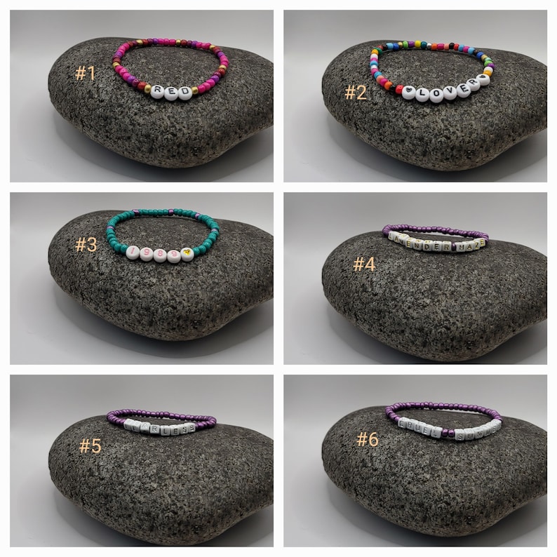 K&ouml;nnte beinhalten: Sechs bunte Perlenarmb&auml;nder mit verschiedenen W&ouml;rtern, die in wei&szlig;en Buchstaben ausgeschrieben sind. Die Armb&auml;nder liegen auf einem grauen Gesteinsuntergrund. Die W&ouml;rter sind "RED", "LOVER", "1985", "LENDERHAZE", "BLESS" und "CRUEL SUN".