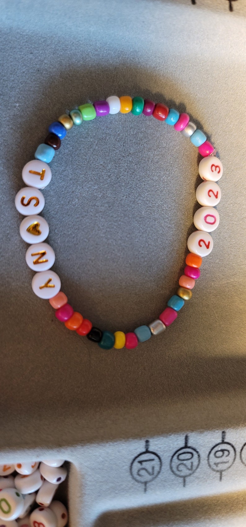 K&ouml;nnte beinhalten: Ein farbenfrohes Perlenarmband mit wei&szlig;en Perlen, die "SONY" buchstabieren, mit einem goldenen Herzen zwischen dem "O" und dem "N" und wei&szlig;en Perlen, die "2023" in Rot buchstabieren.