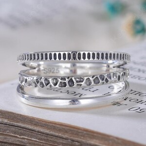 May include: A multi-band silver ring featuring three distinct layers: a top band with vertical grooves, a middle band with a textured, hammered finish, and a smooth bottom band. The inner surface of the ring is clearly stamped with the text S925.
