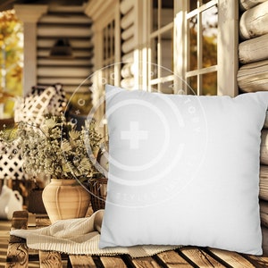 May include: A white pillow sits on a wooden porch with a rustic log cabin background. The pillow is blank and ready for customization.