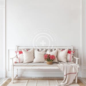 May include: A white bench with a distressed finish, featuring red and white patterned pillows and a throw blanket. A bouquet of pink flowers in a woven basket sits on the bench.