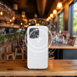 May include: White iPhone case with a black camera lens and a logo that says "Mock-Up Factor Quality Styled Images".