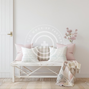 Op de afbeelding: Een witte bank met een witgeschilderde afwerking en een verweerde look. De bank is versierd met een roze en witte geruite deken en verschillende kussens in tinten roze en wit. Een vaas met roze bloemen staat op de vloer achter de bank.