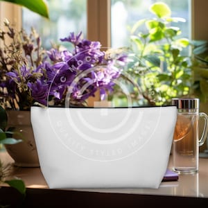 May include: White zippered pouch with black trim, sitting on a wooden surface next to a glass tea bottle and a purple flower arrangement. The pouch has the text "QUALITY STYLED IMAGES" printed on it.