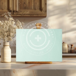 May include: A light blue sign with a wooden easel stand. The sign is blank and ready for your message. The sign is sitting on a white marble countertop in a kitchen setting.