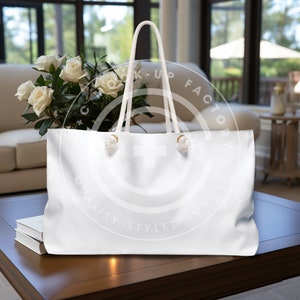May include: White canvas tote bag with rope handles and gold metal accents. The bag is sitting on a wooden table with a bouquet of white roses in the background.