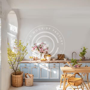 Op de afbeelding: Een lichtblauwe keuken met witte kasten, een houten tafel met rieten stoelen en een groot raam waar zonlicht doorheen schijnt. Er staan planten en bloemen op het aanrecht en de tafel.