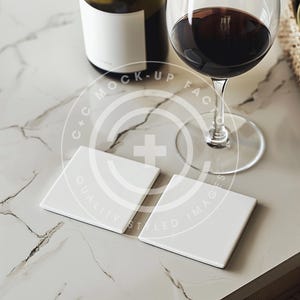 May include: Two white square ceramic coasters with the text "C+C MOCK-UP FACES STYLED IMAGES QUALITY" on them. The coasters are on a marble surface with a glass of red wine and a bottle of wine in the background.