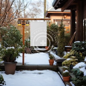Puede incluir: Un cartel blanco en blanco cuelga de un marco de madera frente a un jardín de invierno nevado. El cartel está sujeto a un poste de madera con dos lámparas a cada lado. El cartel está rodeado de vegetación y nieve.