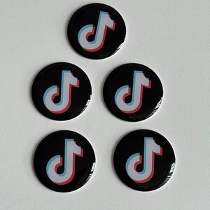 May include: Five black round buttons with the TikTok logo. The logo features a white musical note with a red and blue outline. The buttons are arranged in a triangular pattern against a white background.