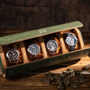 May include: A green leather watch case containing four watches. The case is open, displaying watches with brown leather straps and black faces. The initials "EM" are embossed on the case. The case rests on a wooden surface.