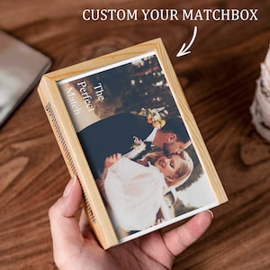 Pode incluir: Uma caixa de fósforos de madeira com uma fotografia de um casal a beijar-se. O texto "The Perfect Match" está impresso na frente. Na parte superior da caixa de fósforos está o texto "CUSTOM YOUR MATCHBOX".