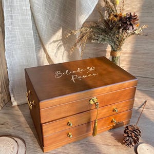 May include: A wooden jewelry box with three drawers and a gold tassel. The box is engraved with the names "Belinda" and "Roman" and a heart symbol.