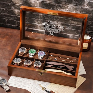 May include: A wooden watch and jewelry display case with a glass top. The case contains several watches with different colored faces, rings, and a pair of sunglasses. The text "DEVY BVKKER" is visible on the glass.